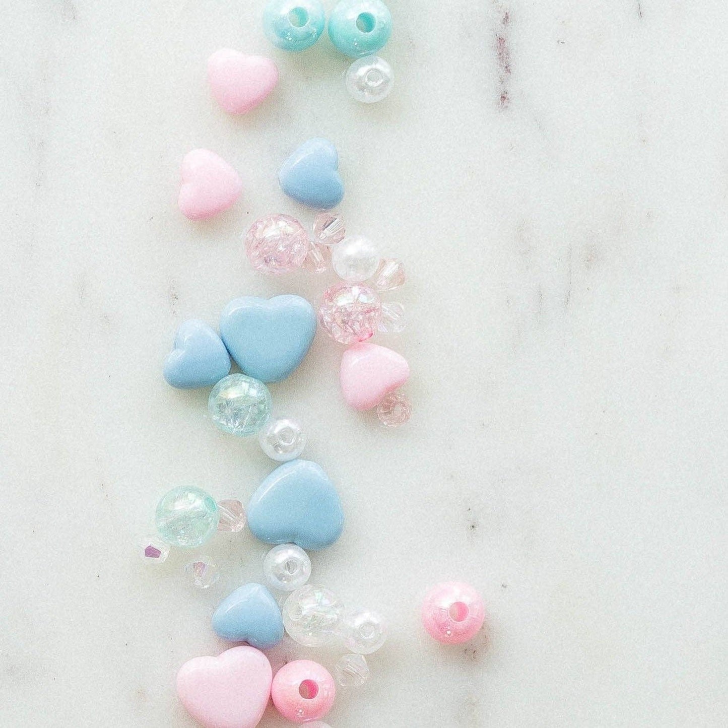 DIY Swiftie friendship bracelet kit featuring light pink and blue heart beads, glitter beads, and clear string. Comes in a silver bag with 'Lover' theme, perfect for creating two custom bracelets. Ideal for Taylor Swift fans and crafting enthusiasts.