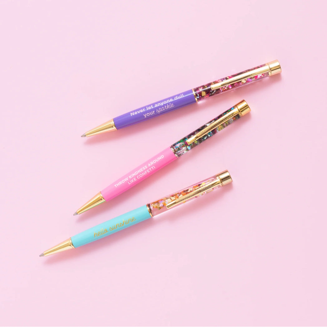 Confetti pen with gold metal accents, imprinted with 'Never let anyone dull your sparkle.' Medium ballpoint pen with black ink and a twist tip. Perfect desk accessory or gift, pairs well with notebooks. Features water-filled liquid inside for extra sparkle.