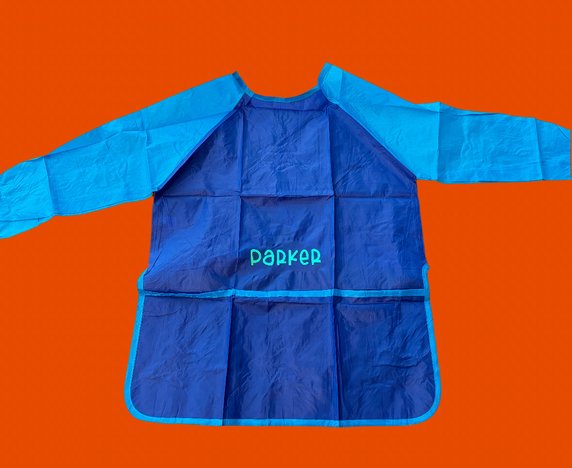 Custom Artist Smock for kids featuring a protective waterproof design, personalized with the child’s name. Ideal for pint-sized Picassos and little artists, this lightweight and durable plastic apron protects clothing from paint and glue. It includes a big front pocket for paint supplies and comes in various colors and font styles.