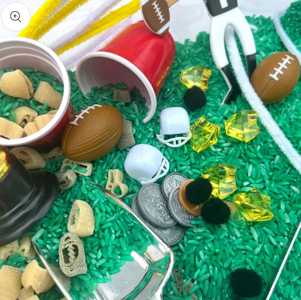 Football-themed sensory kit for kids, perfect for imaginative play. Includes mini footballs, bendable players, trophies, solo cups, foam fingers, helmets, scoops, yellow gems, pom-poms, pipe cleaners, tongs, coins, green rice, and football pasta. Encourages creativity and fine motor skills. Ages 3+, adult supervision recommended. Bin not included. Warning: small parts choking hazard.