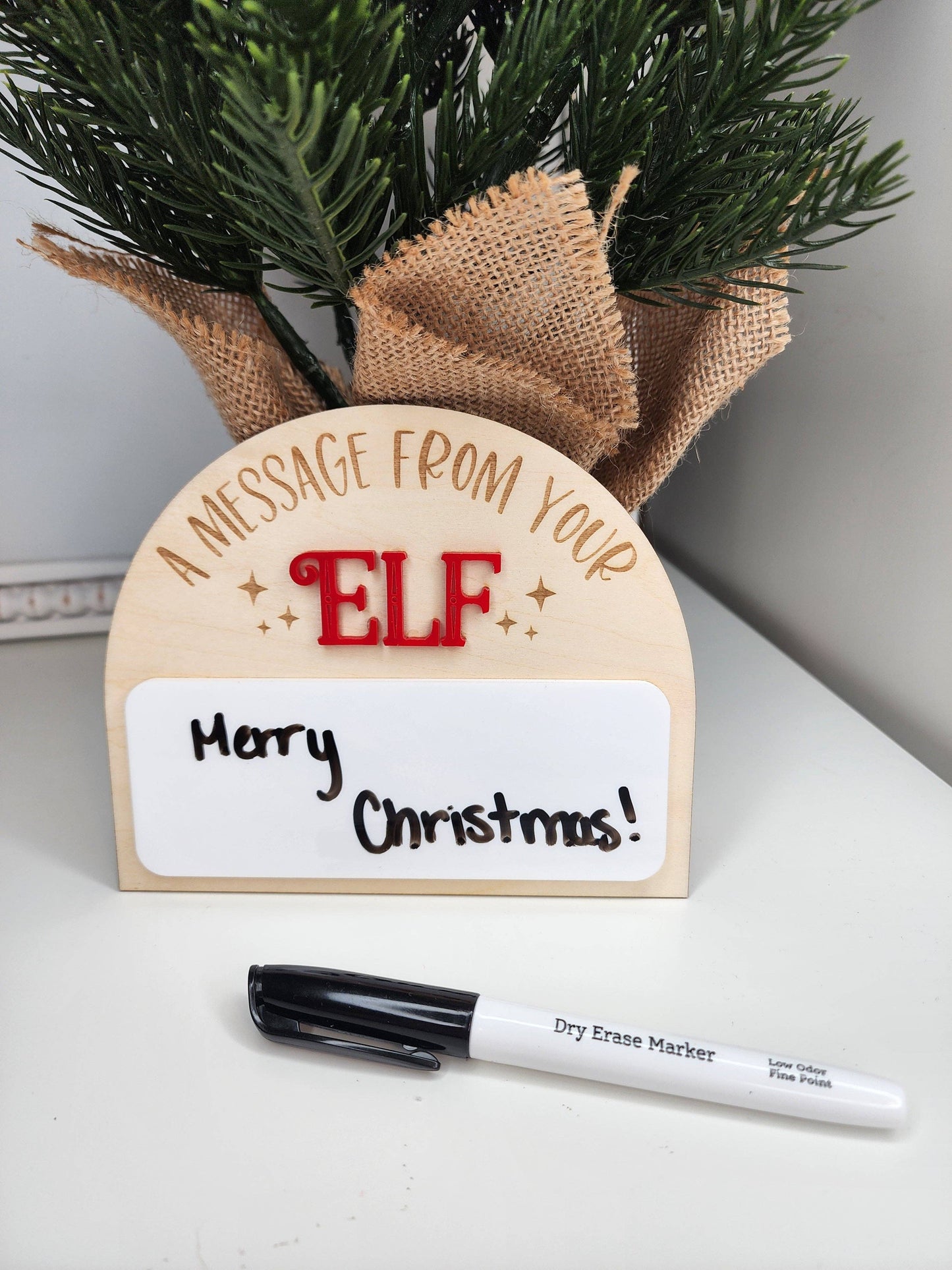 A personalized Elf on the Shelf dry-erase board made from 1/8" birch and acrylic. The board features a laser-cut and engraved design, perfect for adding creative messages from your elf this Christmas. Dry erase marker not included. Slight imperfections may be present due to the handmade nature of the product.