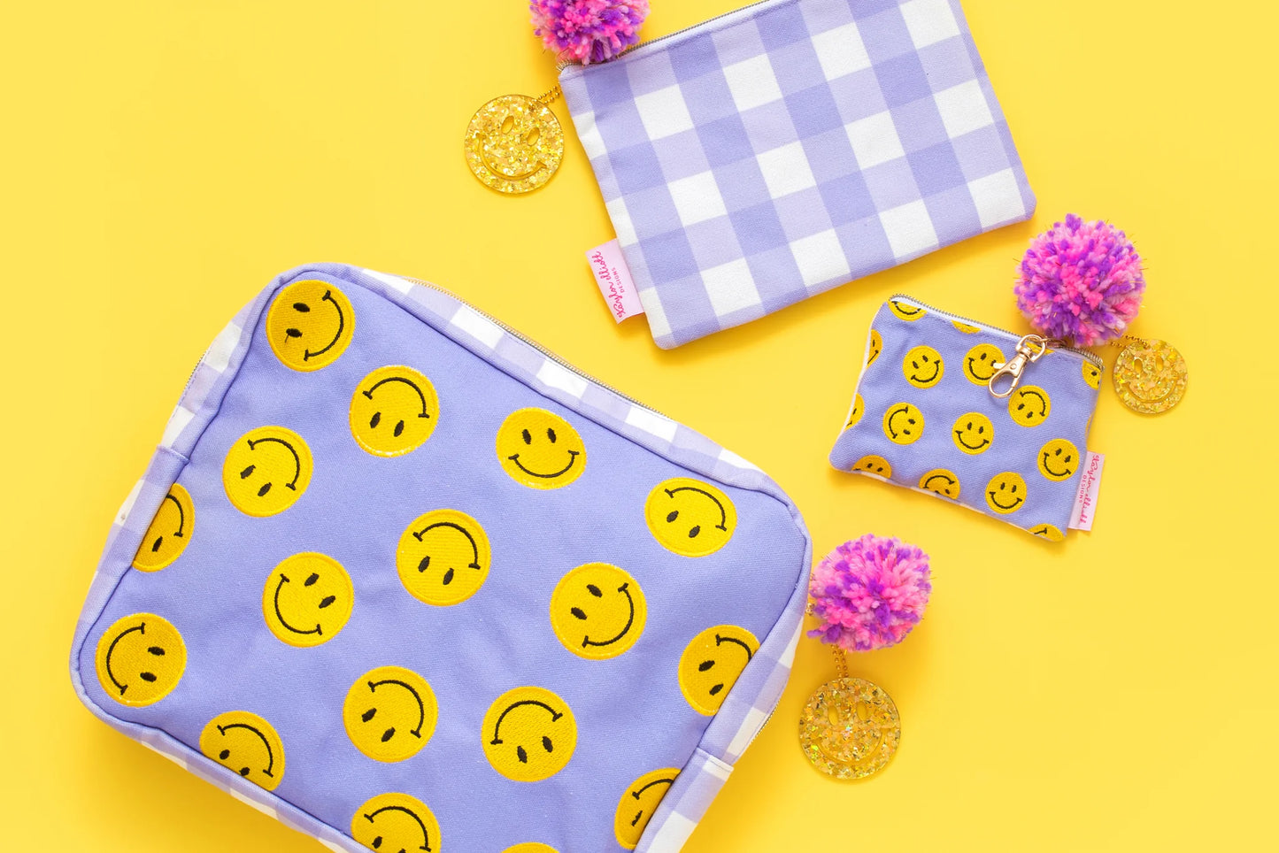 Medium smiley pouches with embroidered design, gold zipper accents, and pom-pom details.