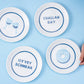 Hanukkah gift set featuring 4 porcelain nosh plates and 4 cotton/linen cocktail napkins, each with playful designs. Perfect for festive meals and gifting. Includes a custom gift box, ideal for holiday celebrations.