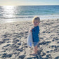 Child on a beach holding a striped bag with ocean in the background