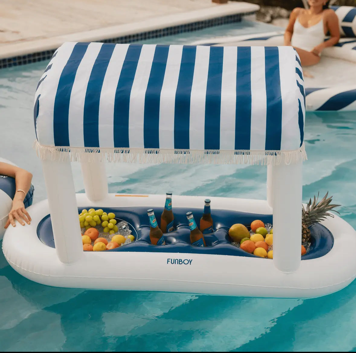 FUNBOY Floating Cabana Bar measuring nearly 6ft long, perfect for outdoor entertainers and summer parties. This inflatable drink station features a navy blue and white cabana stripe fabric sun shade that helps keep drinks and ice cold. With dual circular drink holders for ice or beverages and four additional cup holders, it’s ideal for mixing cocktails in the pool or setting up a pop-up drink station on a table.
