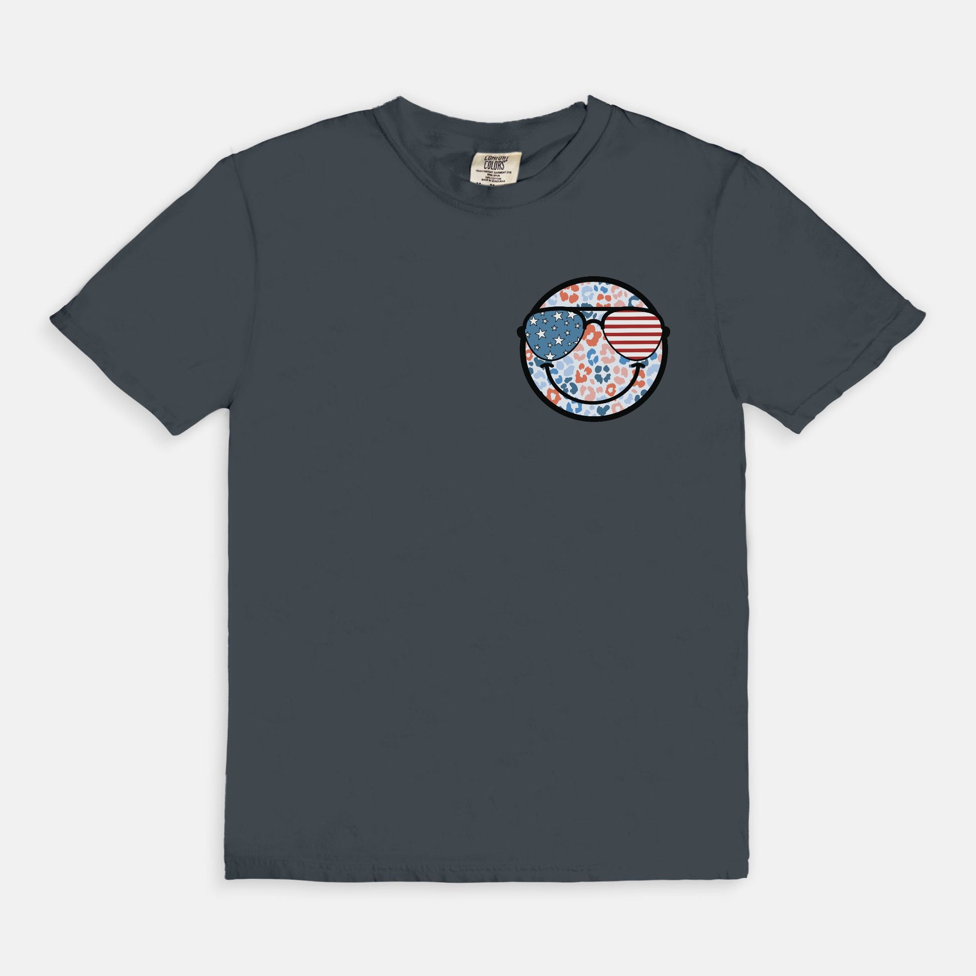 Retro smiley face sunglasses t-shirt featuring a patriotic design with American flag shades. Perfect for 4th of July celebrations, this vintage-style Comfort Colors tee is soft-washed, pre-shrunk, and available in unisex sizes. Show off 90s nostalgia with this fun and comfortable USA flag shirt, ideal for summer BBQs, fireworks, and family gatherings.