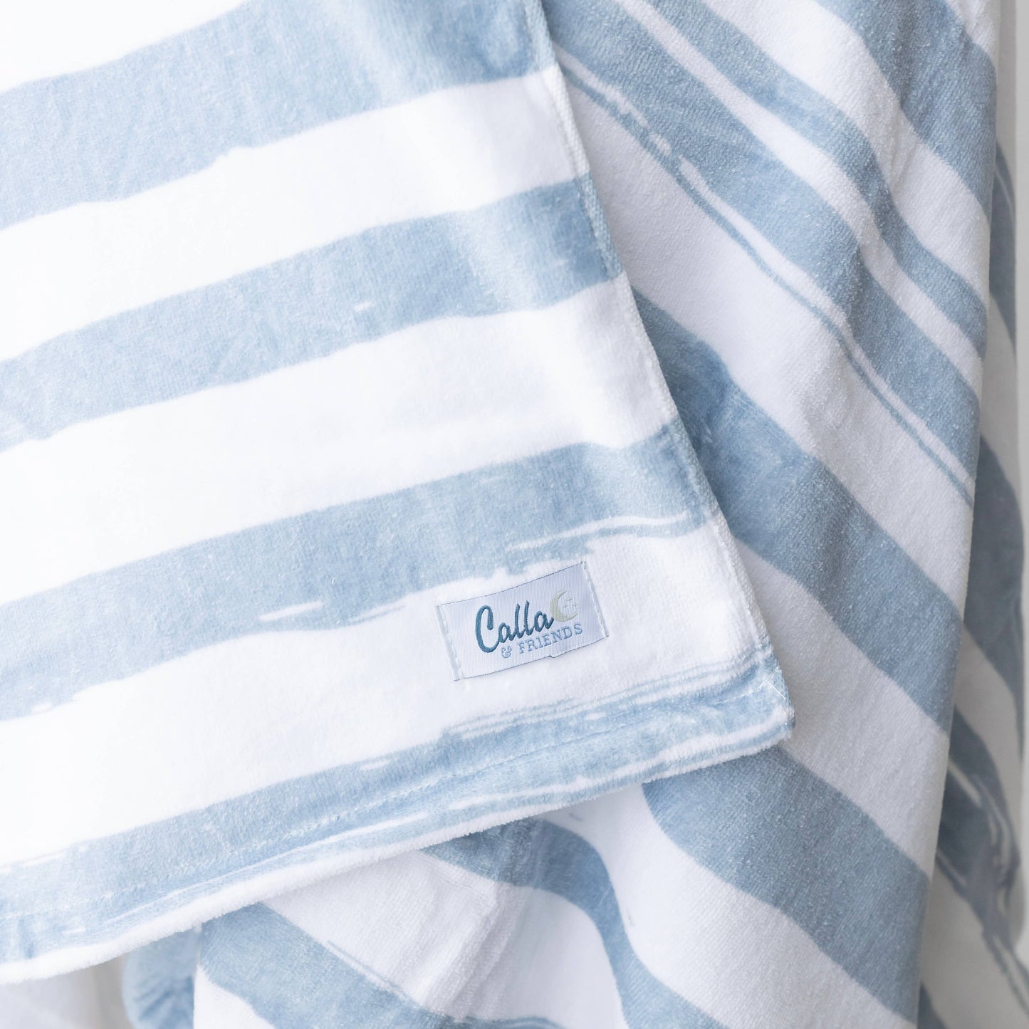 Kenzie Beach Towel Collection in blue stripes beside flip-flops