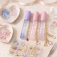 Three small bottles with colorful contents and keychains on a light surface with small bowls of beads and charms.