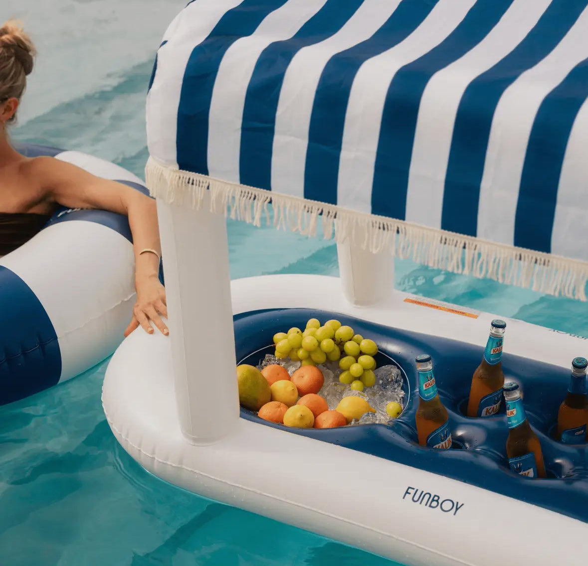FUNBOY Floating Cabana Bar measuring nearly 6ft long, perfect for outdoor entertainers and summer parties. This inflatable drink station features a navy blue and white cabana stripe fabric sun shade that helps keep drinks and ice cold. With dual circular drink holders for ice or beverages and four additional cup holders, it’s ideal for mixing cocktails in the pool or setting up a pop-up drink station on a table.