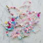 Aquamarine mermaid jewelry kit featuring alphabet beads, shell beads, iridescent star and heart beads, a mermaid tail charm, and pink and clear string. Perfect for creating your own bracelets or necklaces. Made by women-owned small STACKS. Warning: small parts.