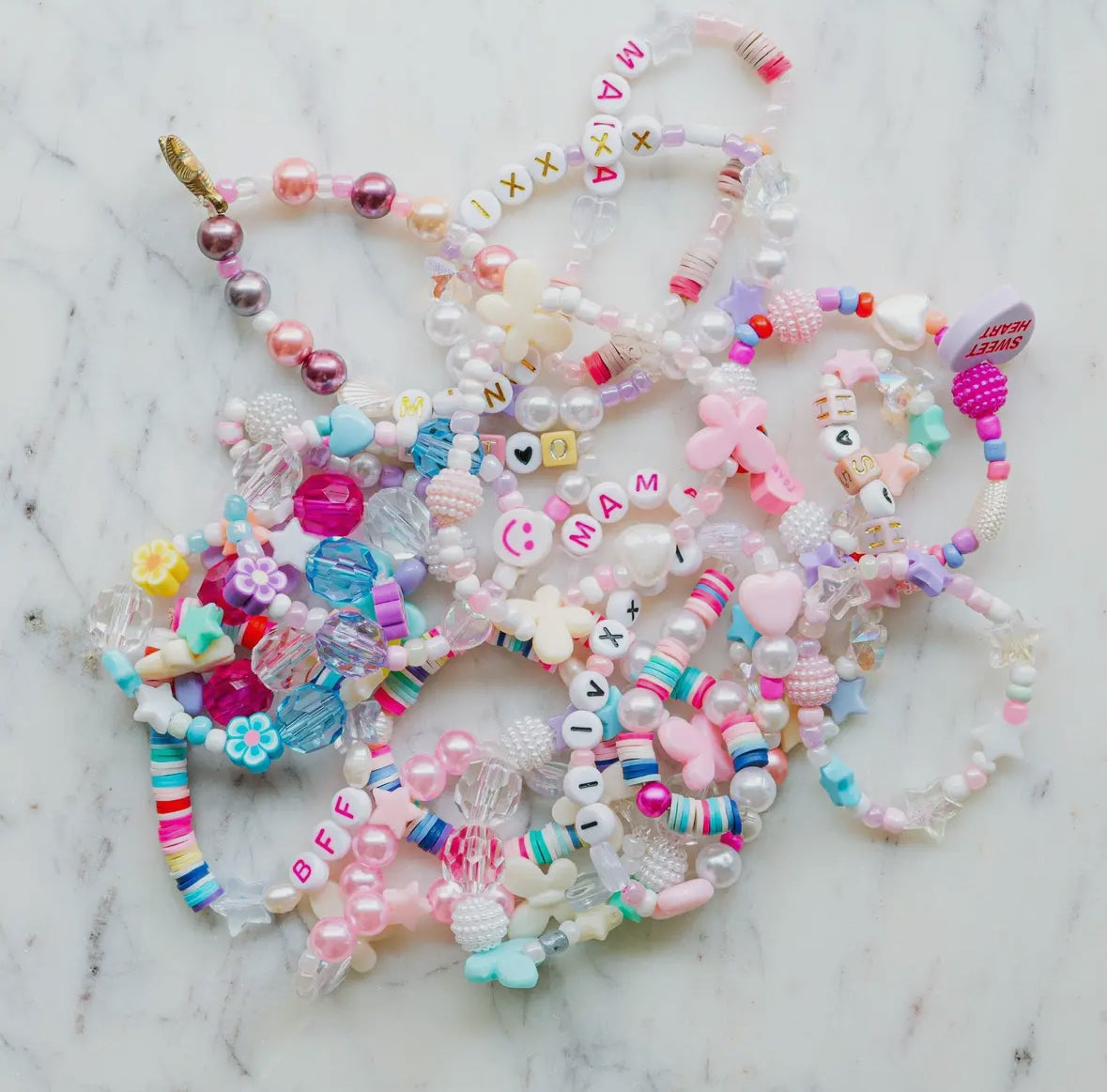 Aquamarine mermaid jewelry kit featuring alphabet beads, shell beads, iridescent star and heart beads, a mermaid tail charm, and pink and clear string. Perfect for creating your own bracelets or necklaces. Made by women-owned small STACKS. Warning: small parts.