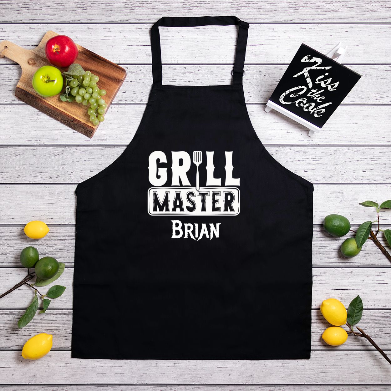 Personalized black kitchen apron with slider neck adjustment for easy sizing. Made from a 7.5 oz poly-cotton blend, featuring a one-sided 10.25"x10.25" design. Machine-washable for convenience, perfect for chefs and home cooks. Add your name for customization.