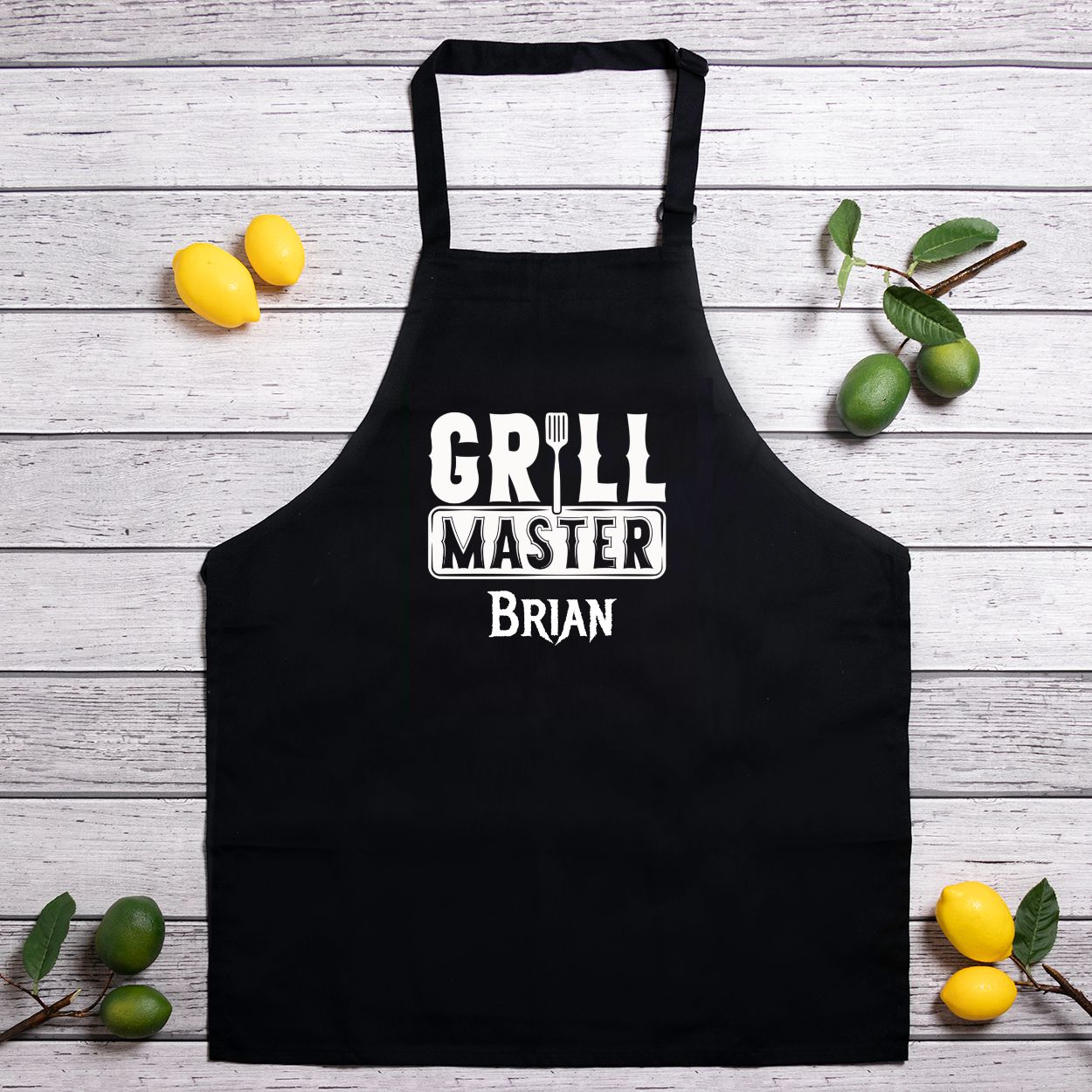 Personalized black kitchen apron with slider neck adjustment for easy sizing. Made from a 7.5 oz poly-cotton blend, featuring a one-sided 10.25"x10.25" design. Machine-washable for convenience, perfect for chefs and home cooks. Add your name for customization.