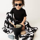 Child wearing sunglasses sitting on a black and white patterned blanket with toys around