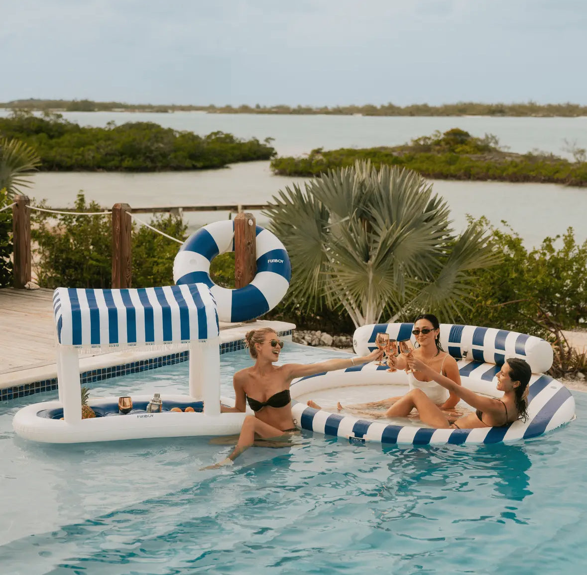 FUNBOY Floating Cabana Bar measuring nearly 6ft long, perfect for outdoor entertainers and summer parties. This inflatable drink station features a navy blue and white cabana stripe fabric sun shade that helps keep drinks and ice cold. With dual circular drink holders for ice or beverages and four additional cup holders, it’s ideal for mixing cocktails in the pool or setting up a pop-up drink station on a table.