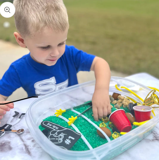 Football-themed sensory kit for kids, perfect for imaginative play. Includes mini footballs, bendable players, trophies, solo cups, foam fingers, helmets, scoops, yellow gems, pom-poms, pipe cleaners, tongs, coins, green rice, and football pasta. Encourages creativity and fine motor skills. Ages 3+, adult supervision recommended. 