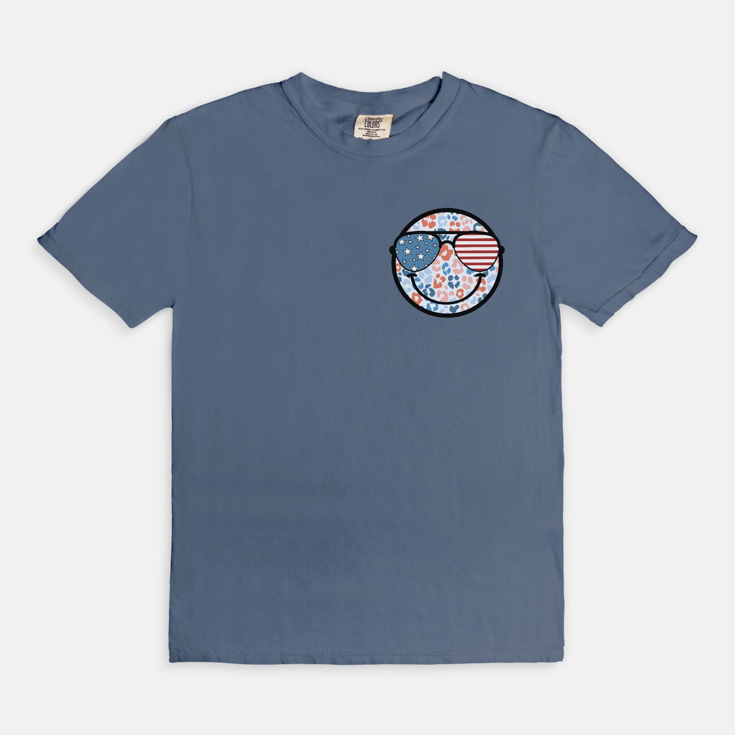Retro smiley face sunglasses t-shirt featuring a patriotic design with American flag shades. Perfect for 4th of July celebrations, this vintage-style Comfort Colors tee is soft-washed, pre-shrunk, and available in unisex sizes. Show off 90s nostalgia with this fun and comfortable USA flag shirt, ideal for summer BBQs, fireworks, and family gatherings.