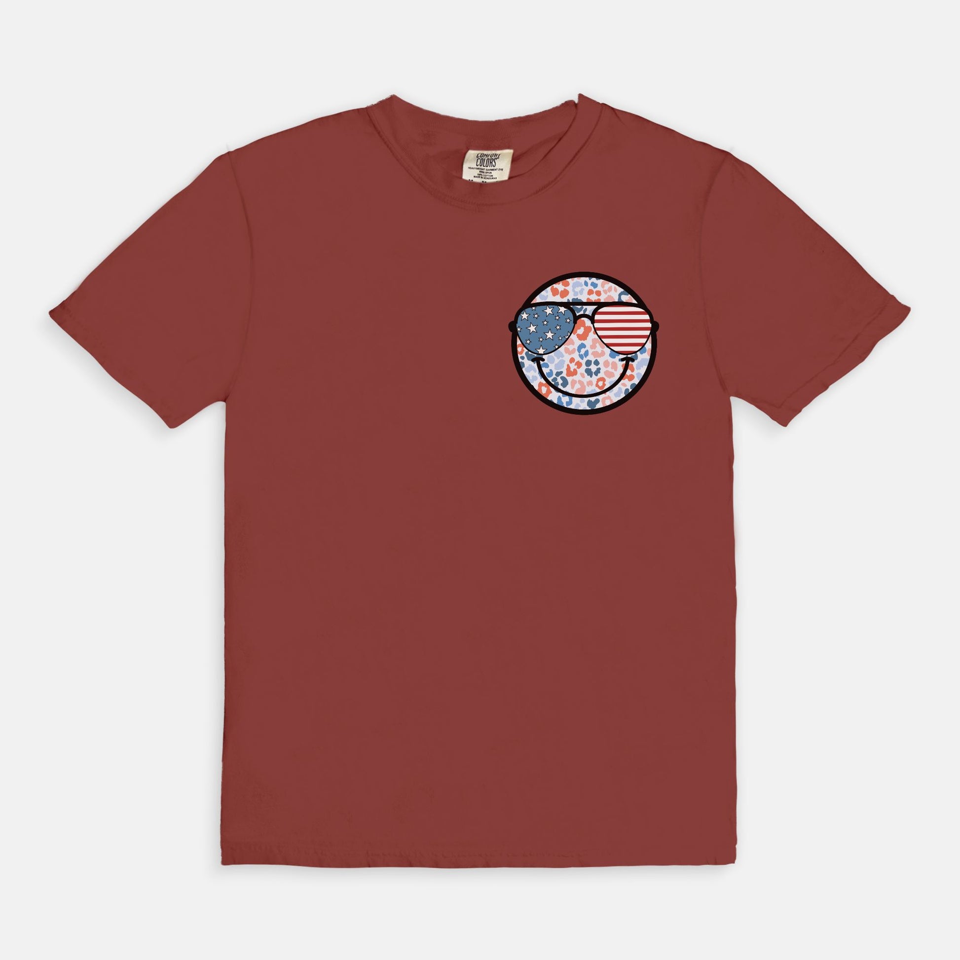 Retro smiley face sunglasses t-shirt featuring a patriotic design with American flag shades. Perfect for 4th of July celebrations, this vintage-style Comfort Colors tee is soft-washed, pre-shrunk, and available in unisex sizes. Show off 90s nostalgia with this fun and comfortable USA flag shirt, ideal for summer BBQs, fireworks, and family gatherings.