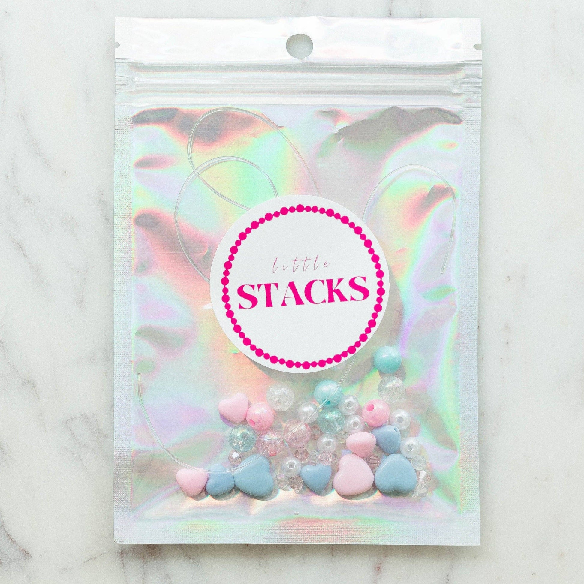 DIY Swiftie friendship bracelet kit featuring light pink and blue heart beads, glitter beads, and clear string. Comes in a silver bag with 'Lover' theme, perfect for creating two custom bracelets. Ideal for Taylor Swift fans and crafting enthusiasts.