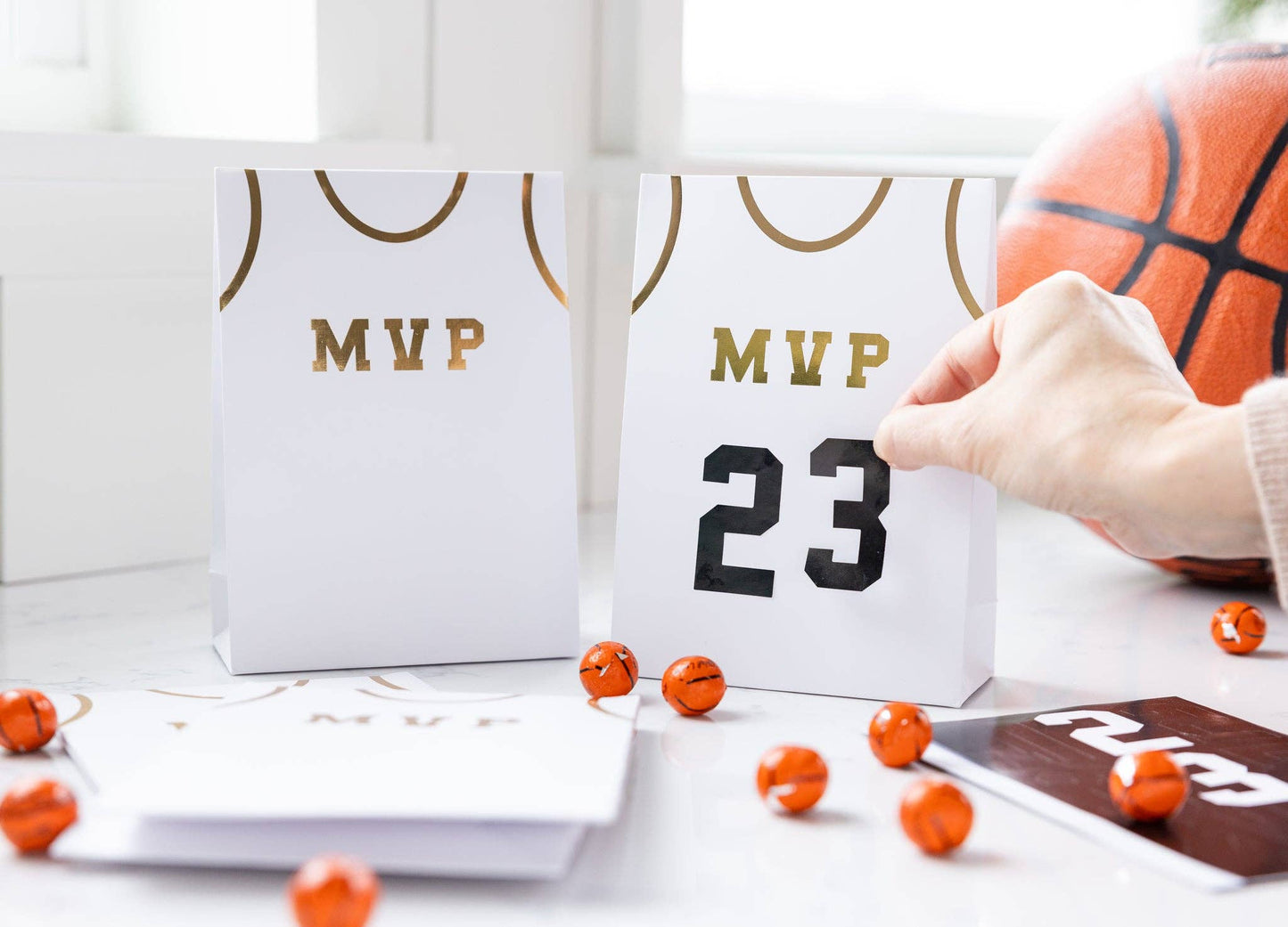 Basketball treat bags set, including 8 jersey-style bags measuring 5" x 8" x 2.5". Features gold number stickers and twine for a fun party accessory. Perfect for kids' basketball-themed parties, ensuring a slam dunk with kids and parents alike.